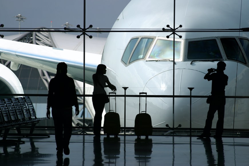 People standing by the windows with a view of a large aircraft in an airport terminal.