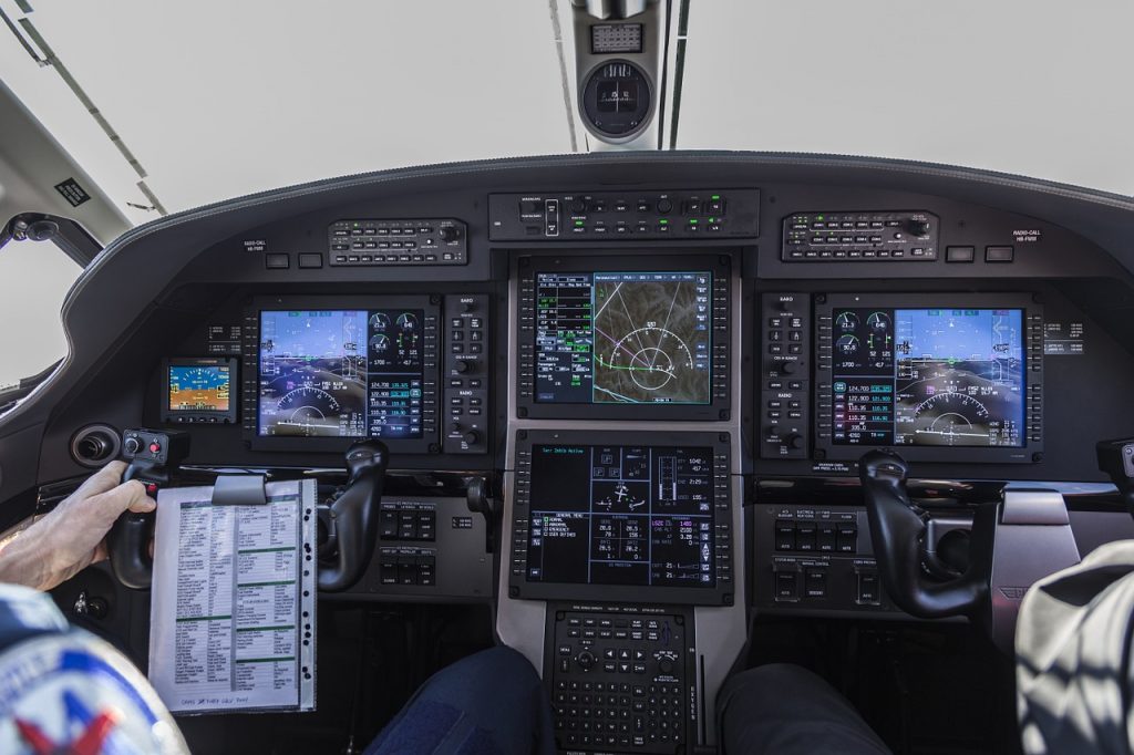 Pilots in a cockpit, holding a list of aviation acronyms by the control column.