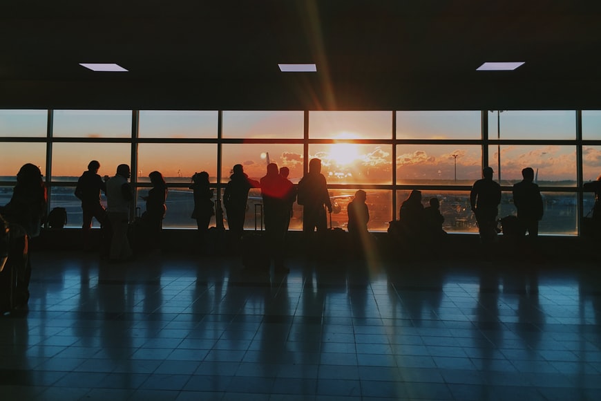 A crowd of passengers at an airport waiting to board a flight at sunset. 