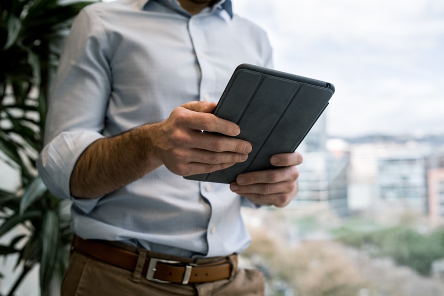 A businessman is doing mobile learning app tasks with an iPad while working near the window of a high-rise building.