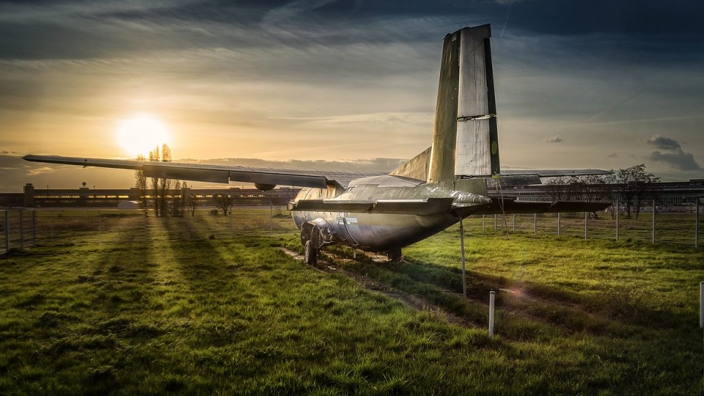An airplane stationed and fenced in on a green field in an airplane graveyard.