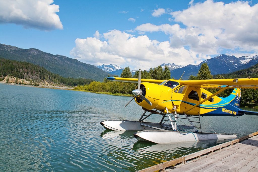 A type of airplanes: a yellow amphibious aircraft parked on a calm surface of water in the mountains.
