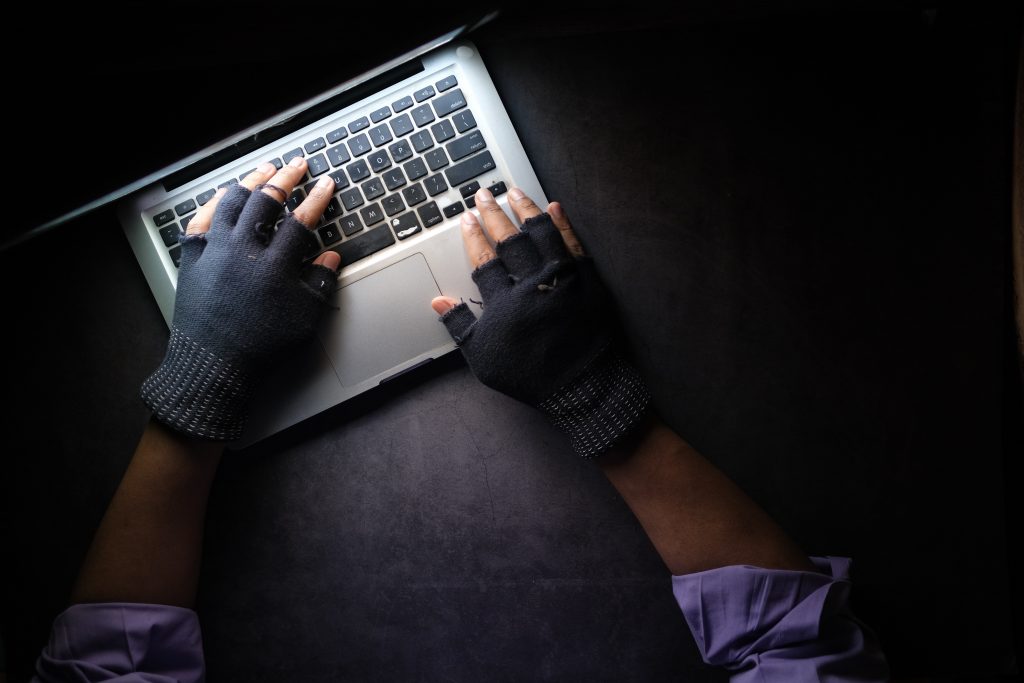 A man with fingerless gloves sitting at a laptop, performing a cyberattack.