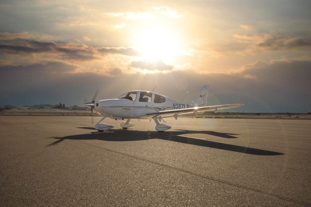 A central view of a Cirrus SR22 aircraft on tarmac while sun is shining over clouds.