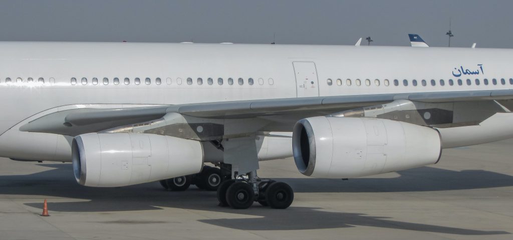 A white plane stationed on the apron of an airport on a cloudy day.