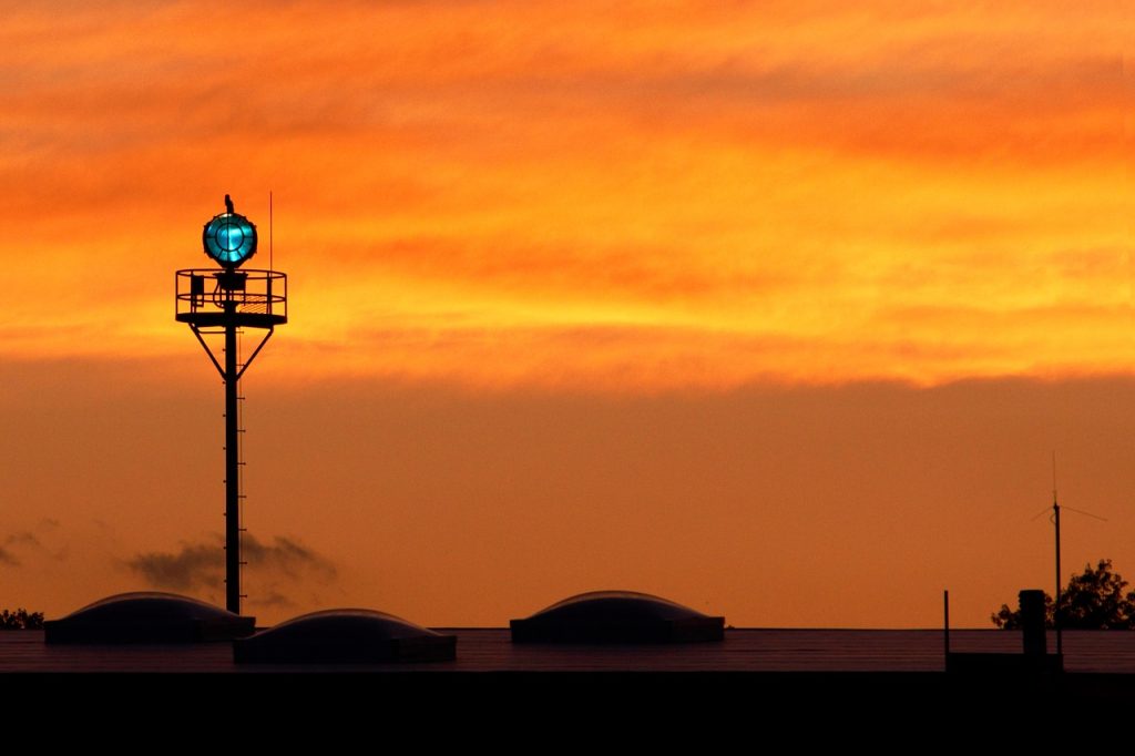 A green airport beacon light in an orange evening sky.