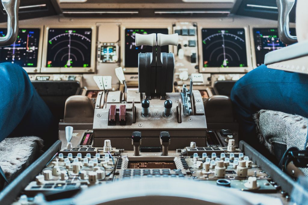 An airplane cockpit and instrument panels as well as two pilots sitting in their seats. 