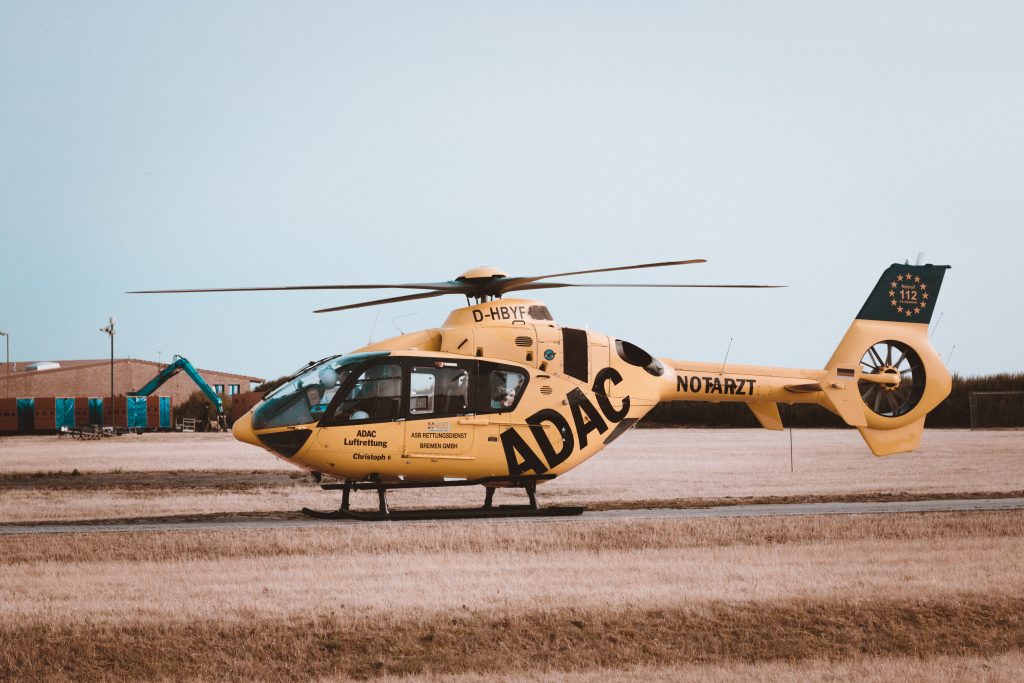 An orange and black helicopter standing on a helipad in a field. 