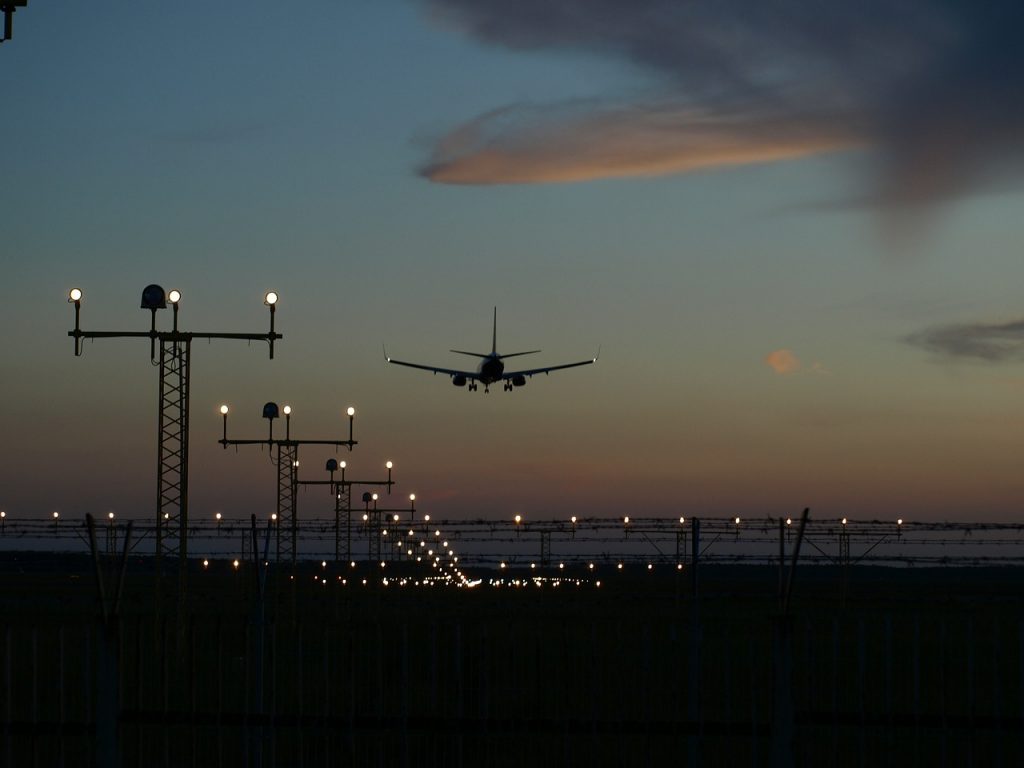 Airport beacon lights illuminating a runway with a landing aircraft in the evening.