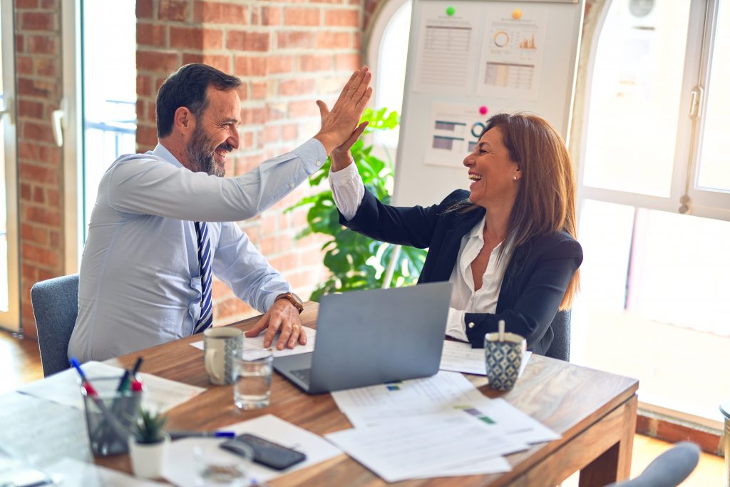 Two colleagues giving each other a high-five while having a meeting an office. 