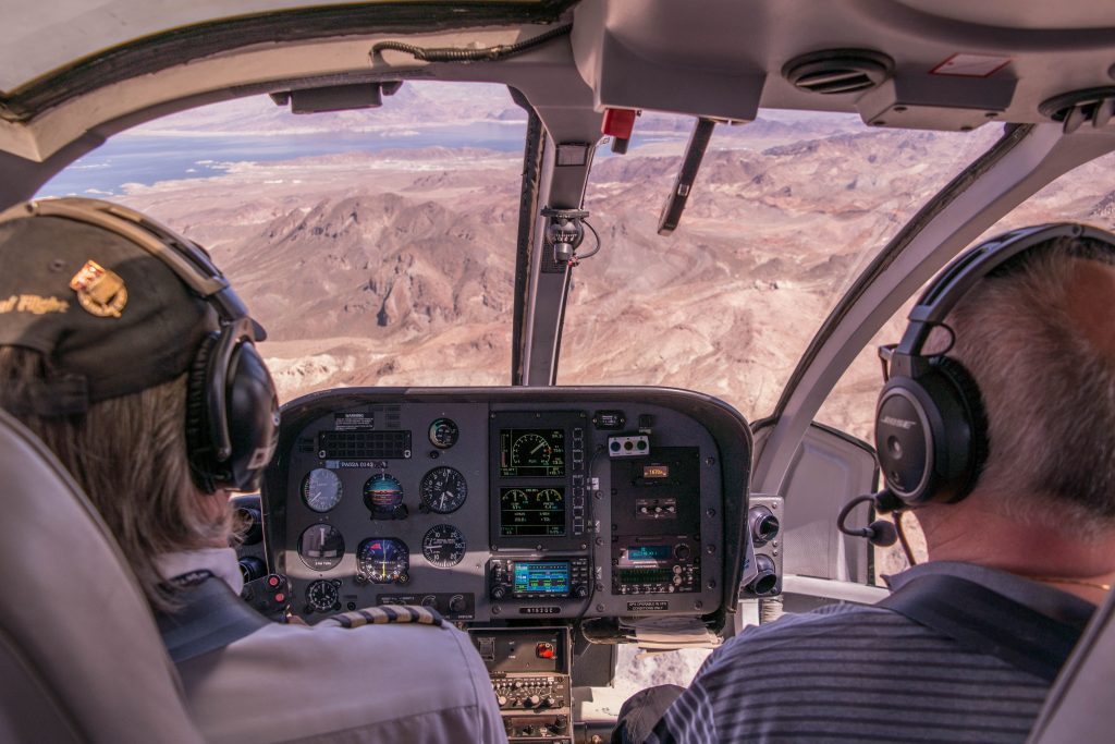 An airplane pilot sitting in a cockpit with a passenger, both wearing headphones.