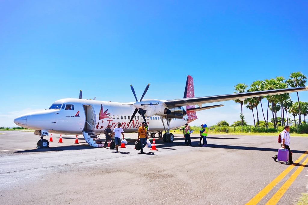 An airplane with propellers and its passengers arrived at a small airport in a tropical country on a bring summer day. 