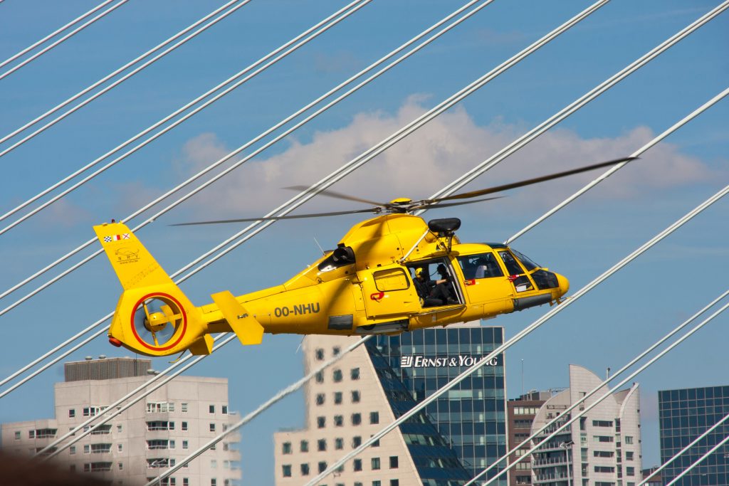 A yellow helicopter flying past bridge suspense in the Netherlands.