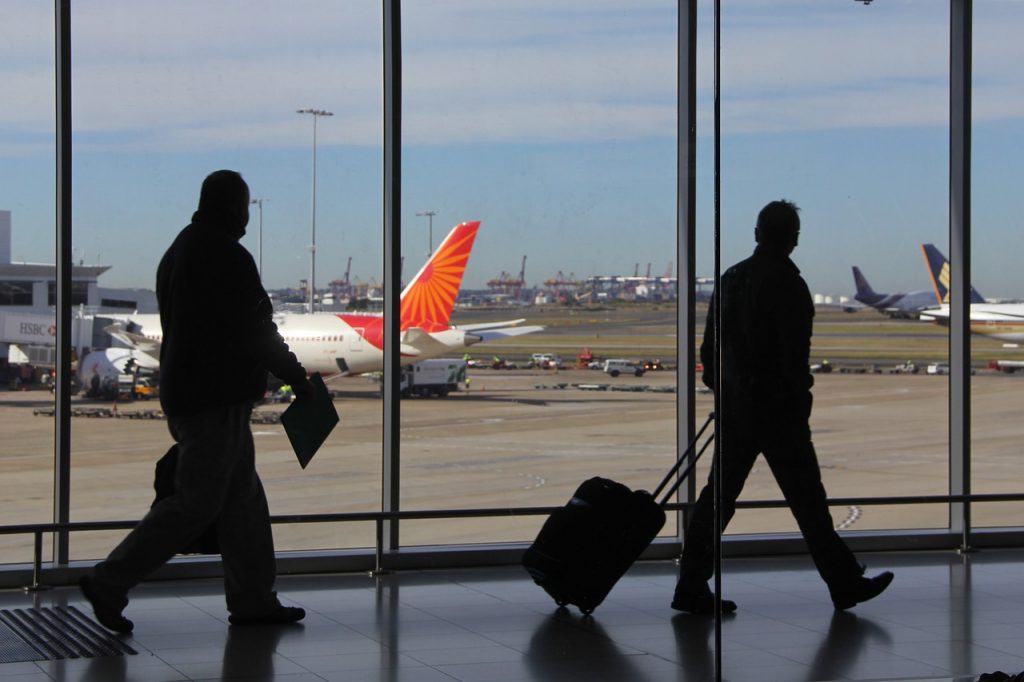 People walking down the airport terminal to their boarding gate, pulling and carrying baggage.