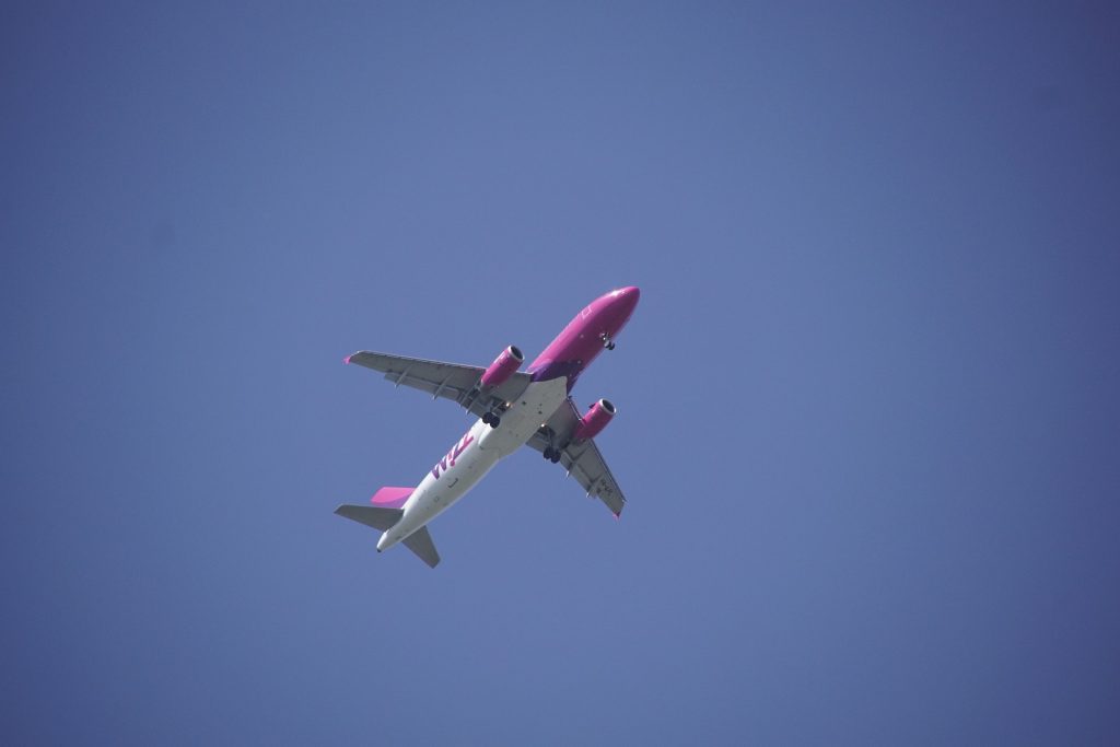 A half white, half pink Wizz Air airplane flying across a blue sky. 