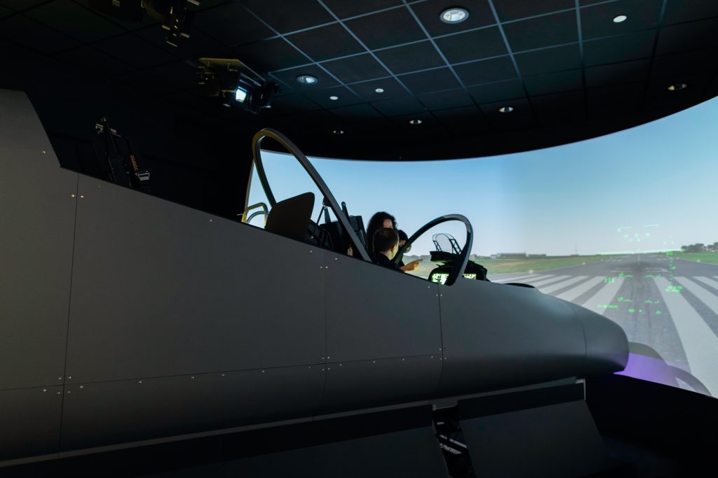 A student in a flight simulator being explained a task by a female aerospace engineer. 