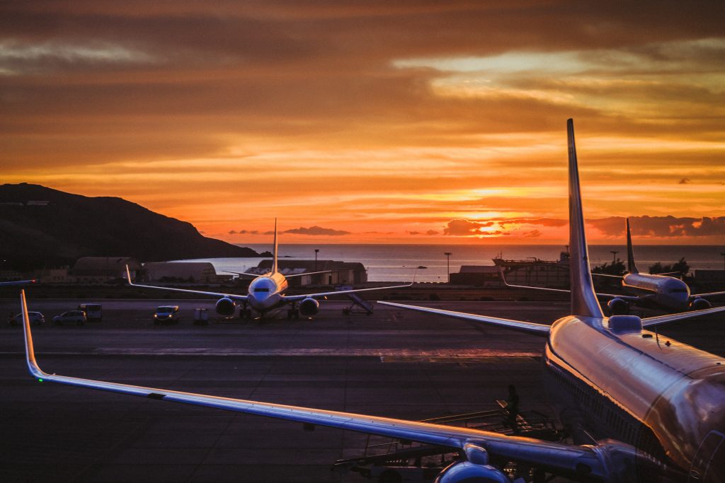 Several airplanes parked at an airport at sunset.