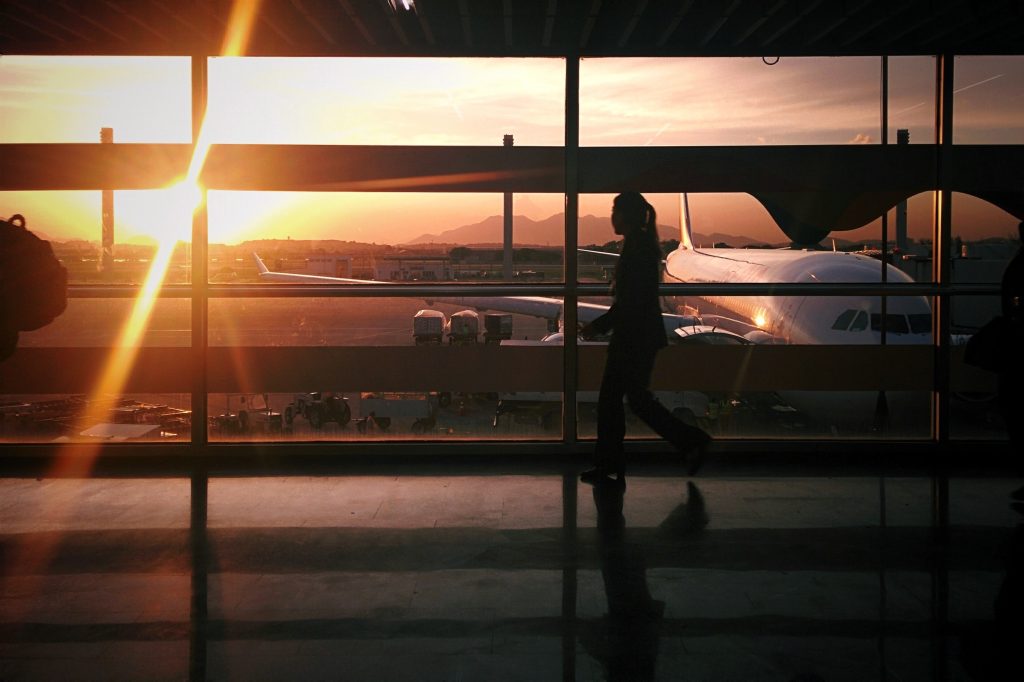 A woman walking to het gate through an airport terminal during sunset.