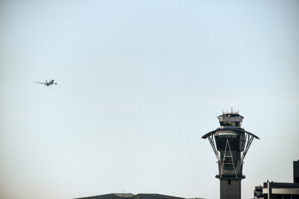 An air traffic control tower and an aircraft approaching the airport to land. 