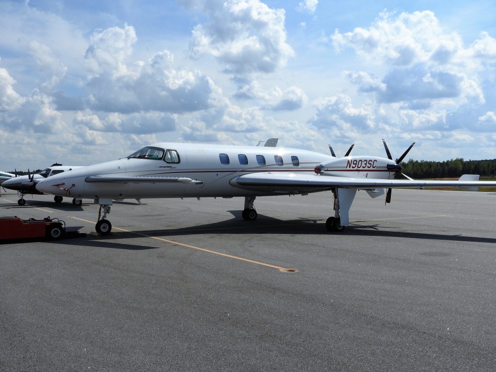 A Beechcraft Starship parked on a tarmac at an airport on a summer day.