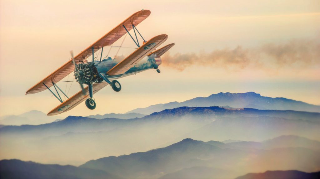 A small bi plane flying through a mountainous region in the evening.