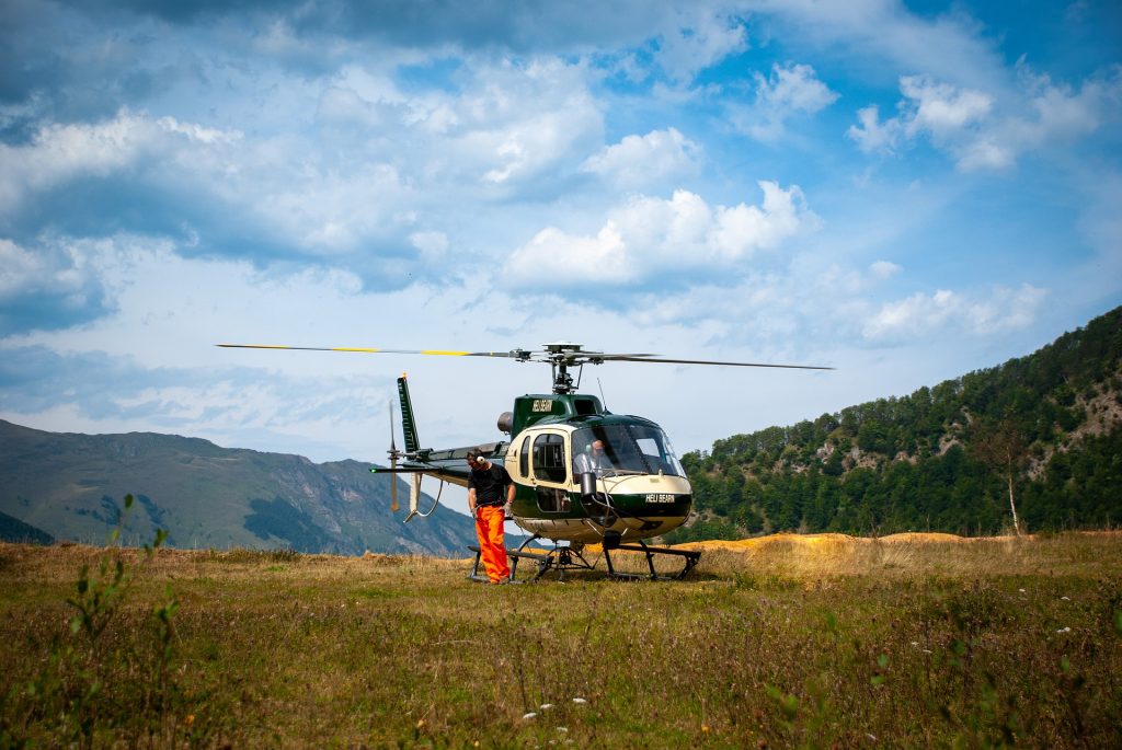 A small helicopter stationed in a grassy field in the mountains. 