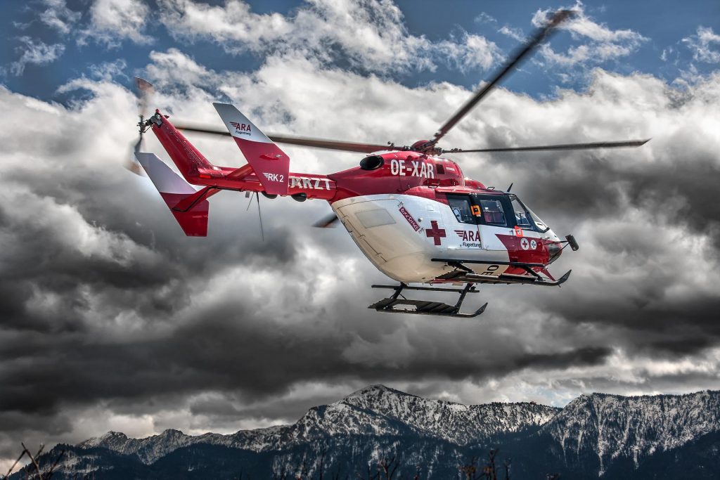 A red and white Swiss helicopter flying over mountains. 