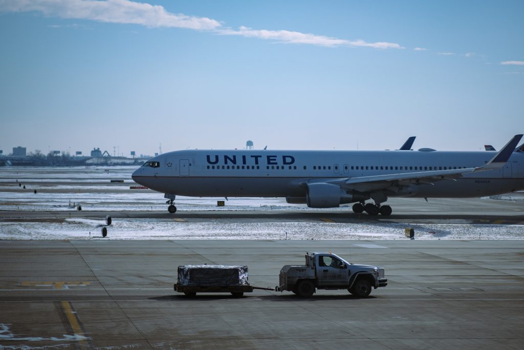 A United airlines aircraft parked at an airport during a day with light snowfall.