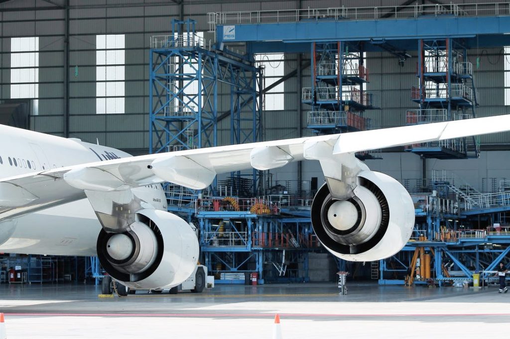 An big white multi-engine airplane stationed for repairs in and MRO hangar.