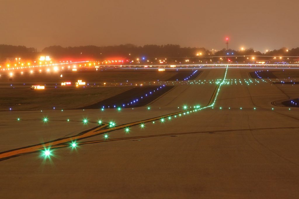 A view of a taxiway at night with visible  green taxiway centerline lights, yellow intersection lights as well as blue taxiway edge lights. 
