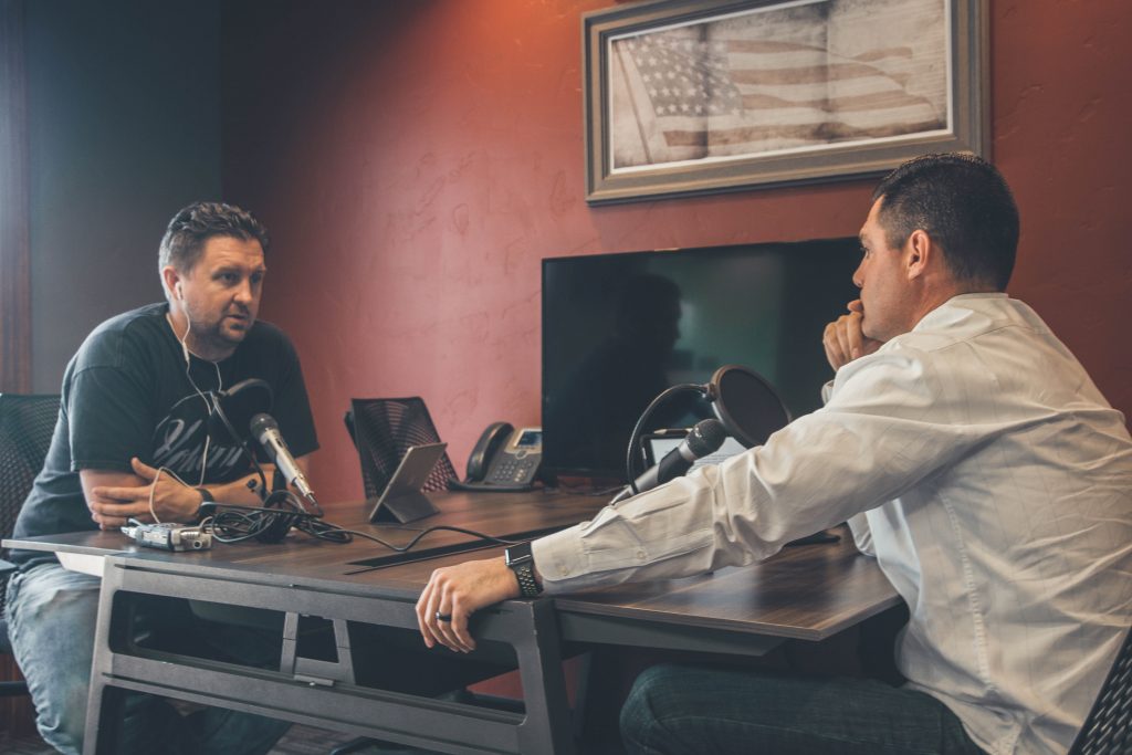 Two men sitting at a desk and recording a podcast.