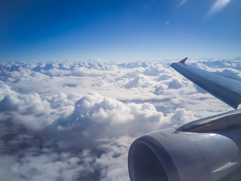 A view of a wing and an engine of an aircraft flying over clouds.