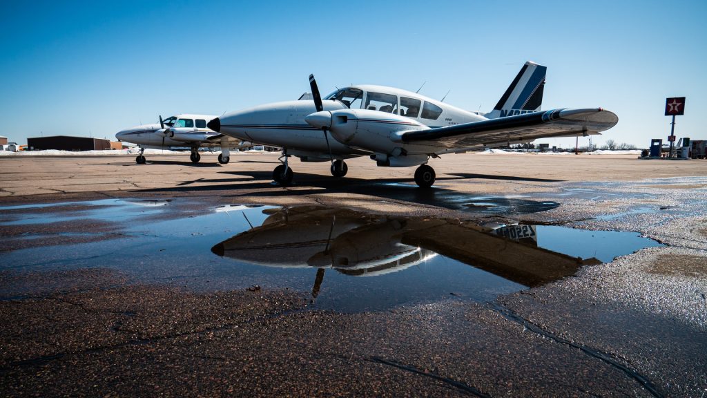 Twin engine piston Piper Aztec plane parked on wet tarmac on a clear day.