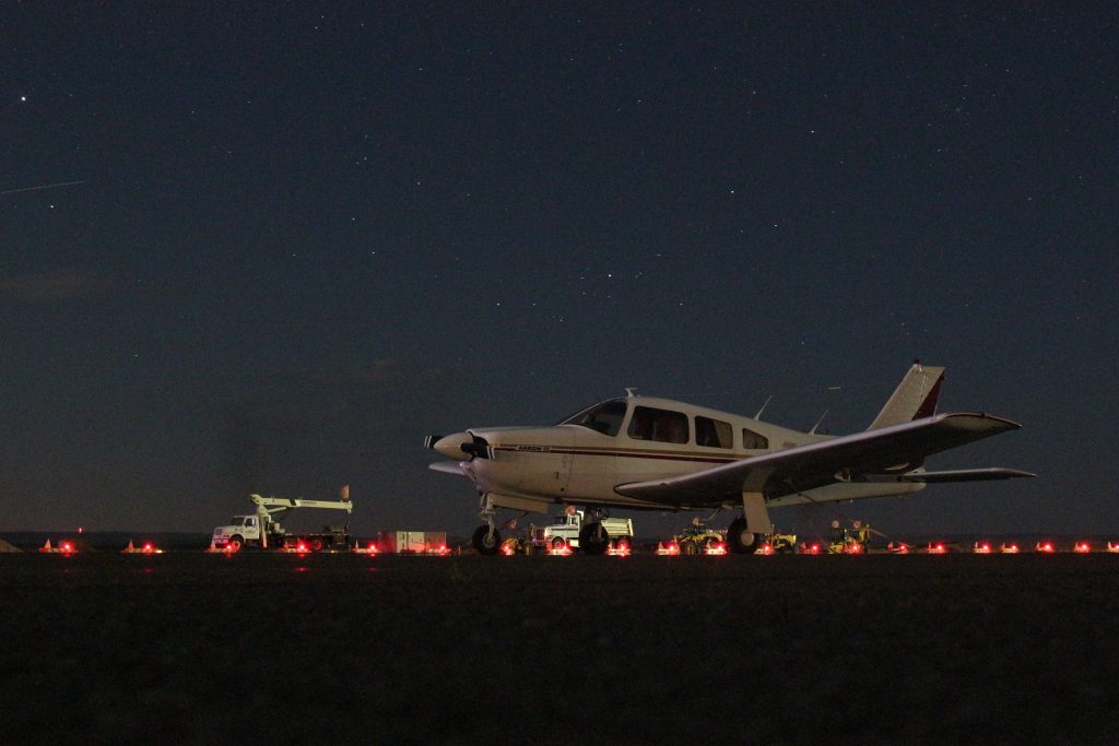 A small personal aircraft has completed a landing at night and is being serviced by airport staff by the runway.
