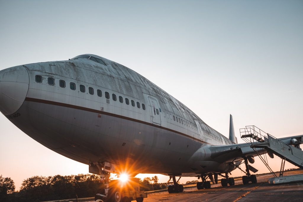 A large commercial aircraft stationed on tarmac with the sun shining from behind it.