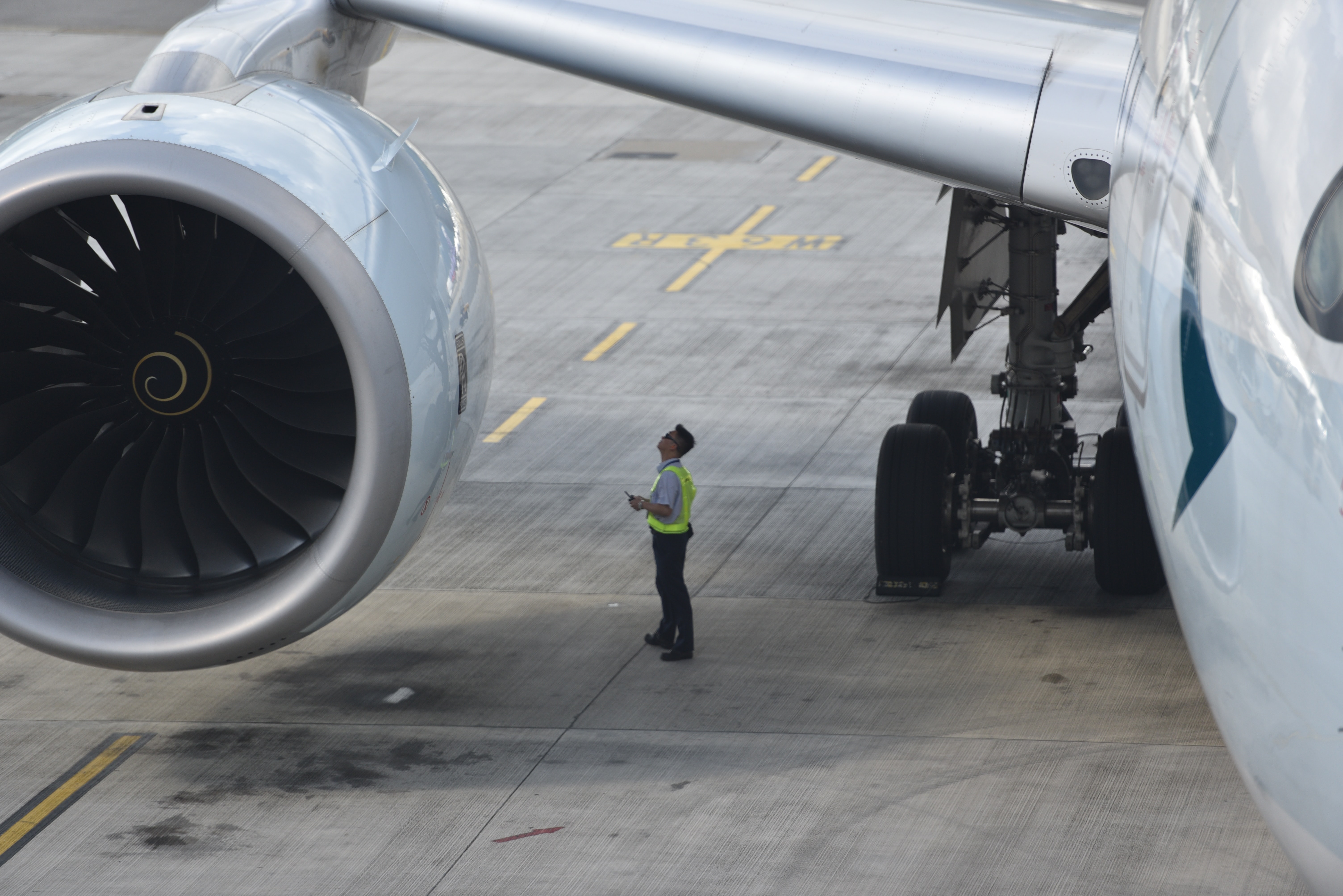 An aircraft mechanic inspecting the engine and wing of an aircraft at an airport. 