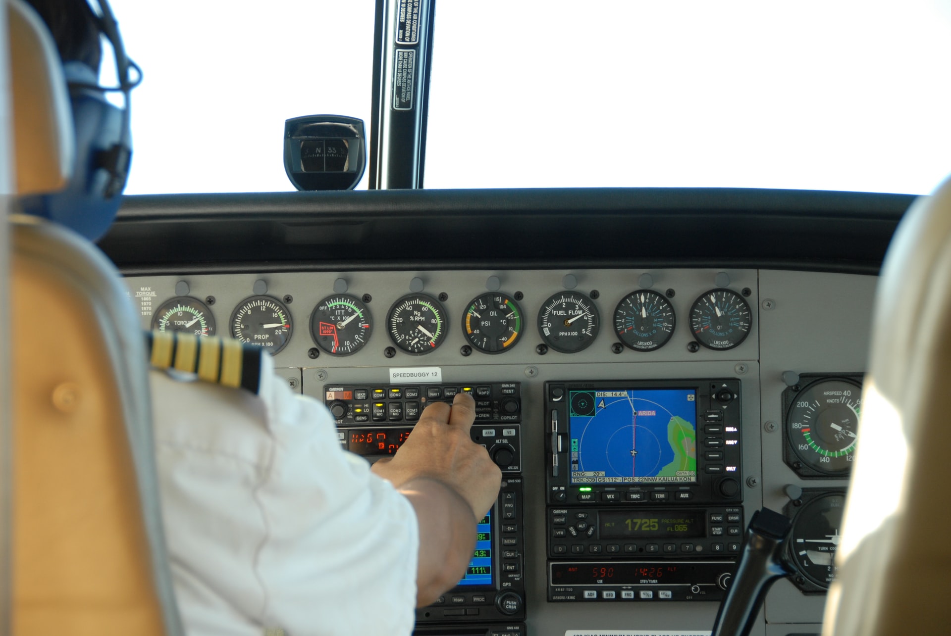 Two pilots in a cockpit of an aircraft with a visible instrument panel and a temperature gauge.