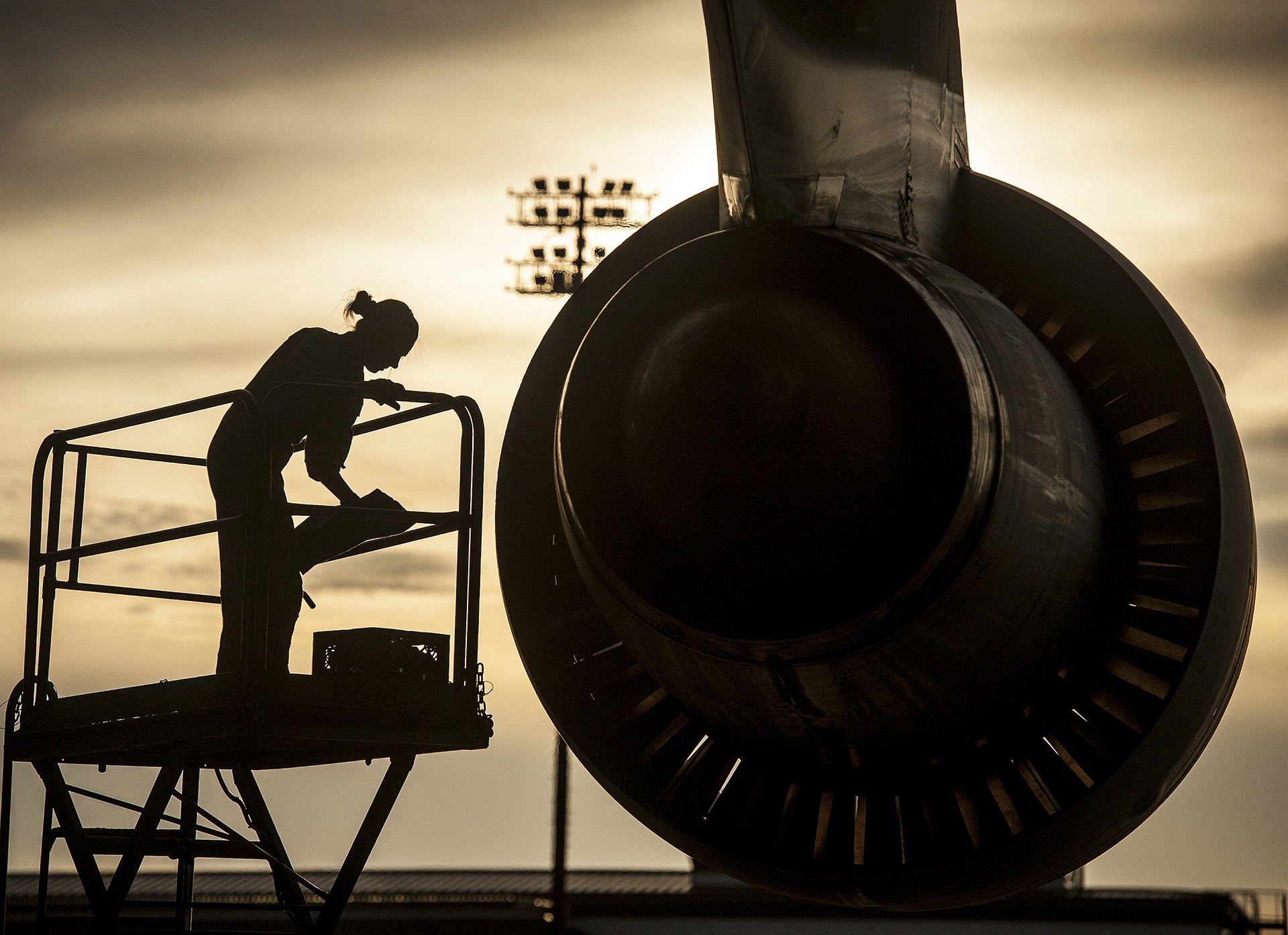 Aircraft maintenance technician is working on an airplane engine while standing on a lift. 