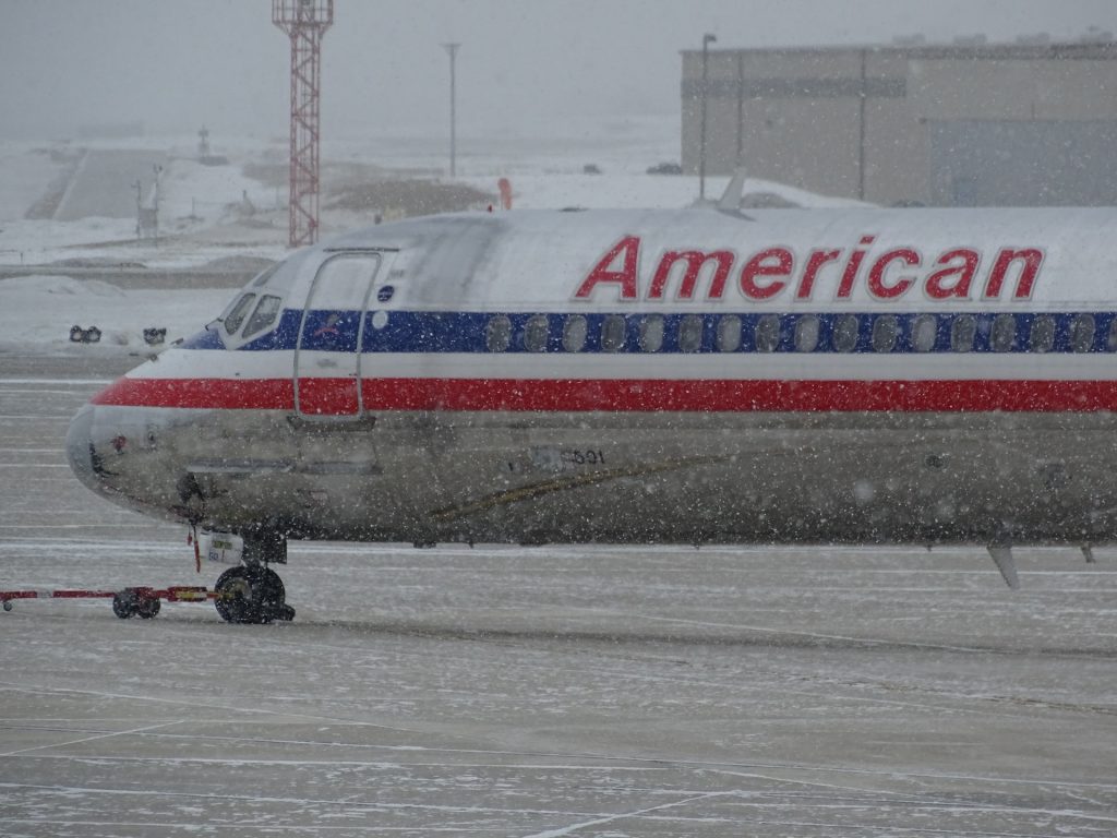 American airlines airplane being towed through heavy winter storm.