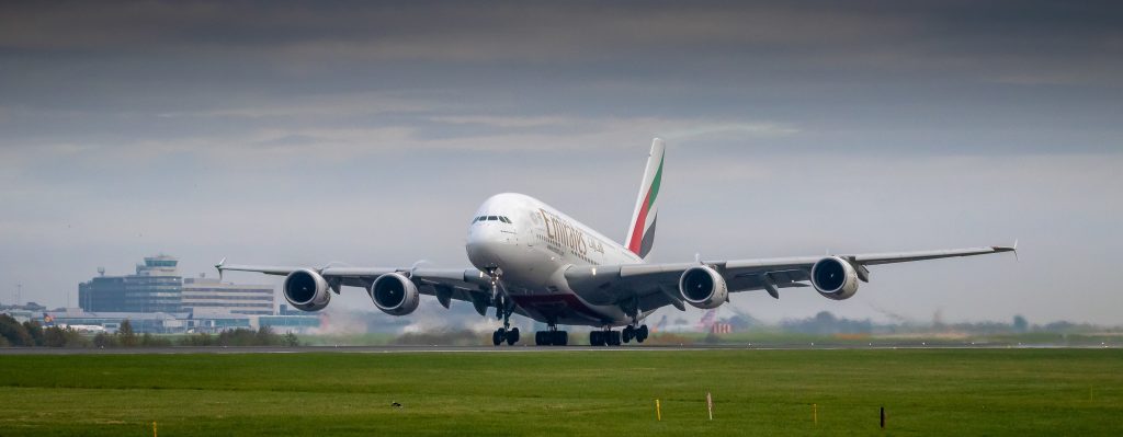 A heavy Emirates aircraft landing on a runway.