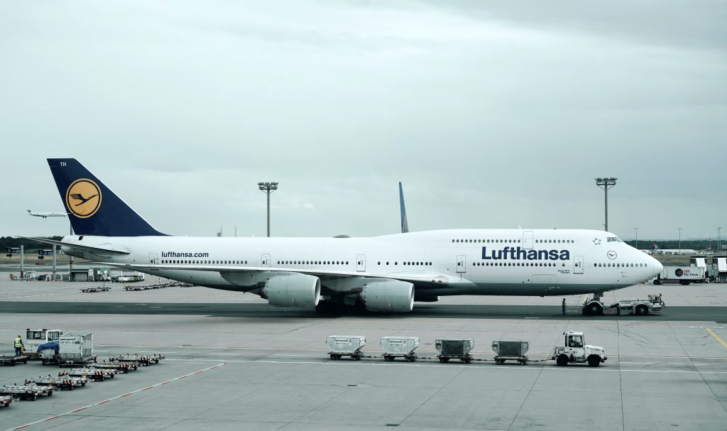 A Lufthansa Boeing 747 Jumbo Jet parked on tarmac at an airport on a cloudy day.
