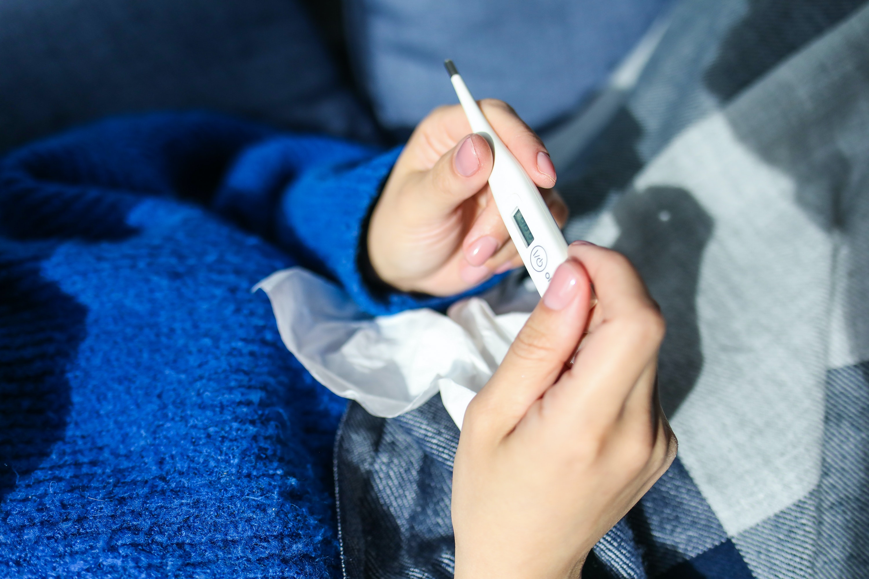 A person with an illness holding a thermometer and a tissue. 