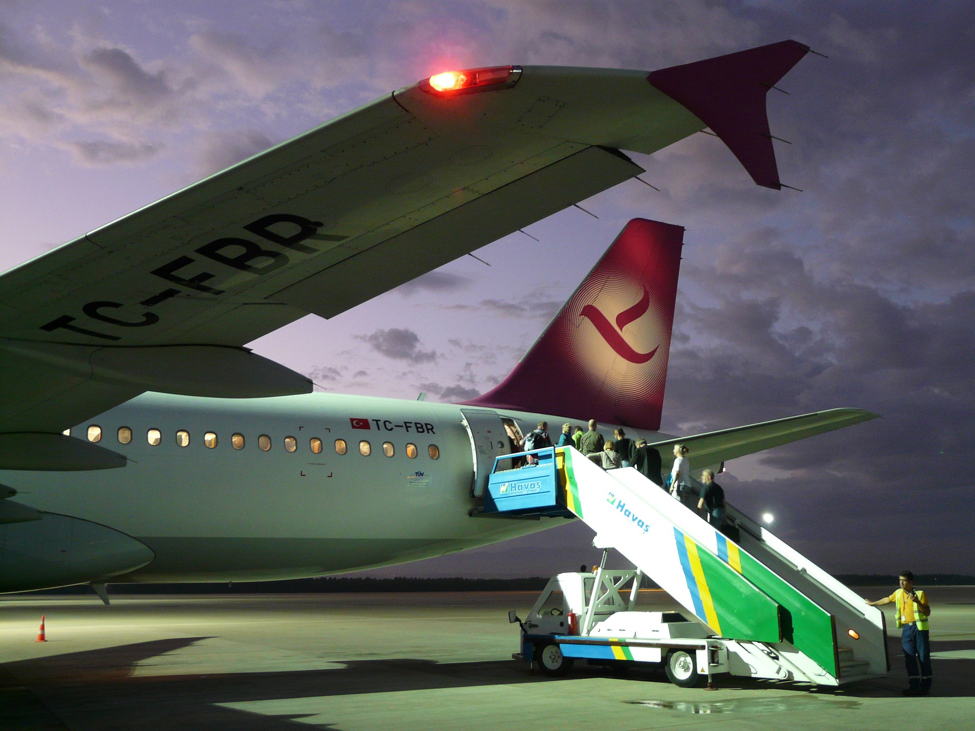 An airplane being boarded at dusk with a visible red position light on the wing.