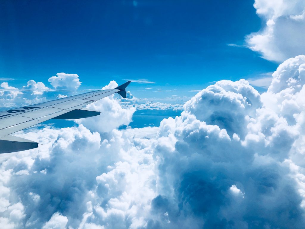 A wing of an airplane on a white cloud and blue sky background.