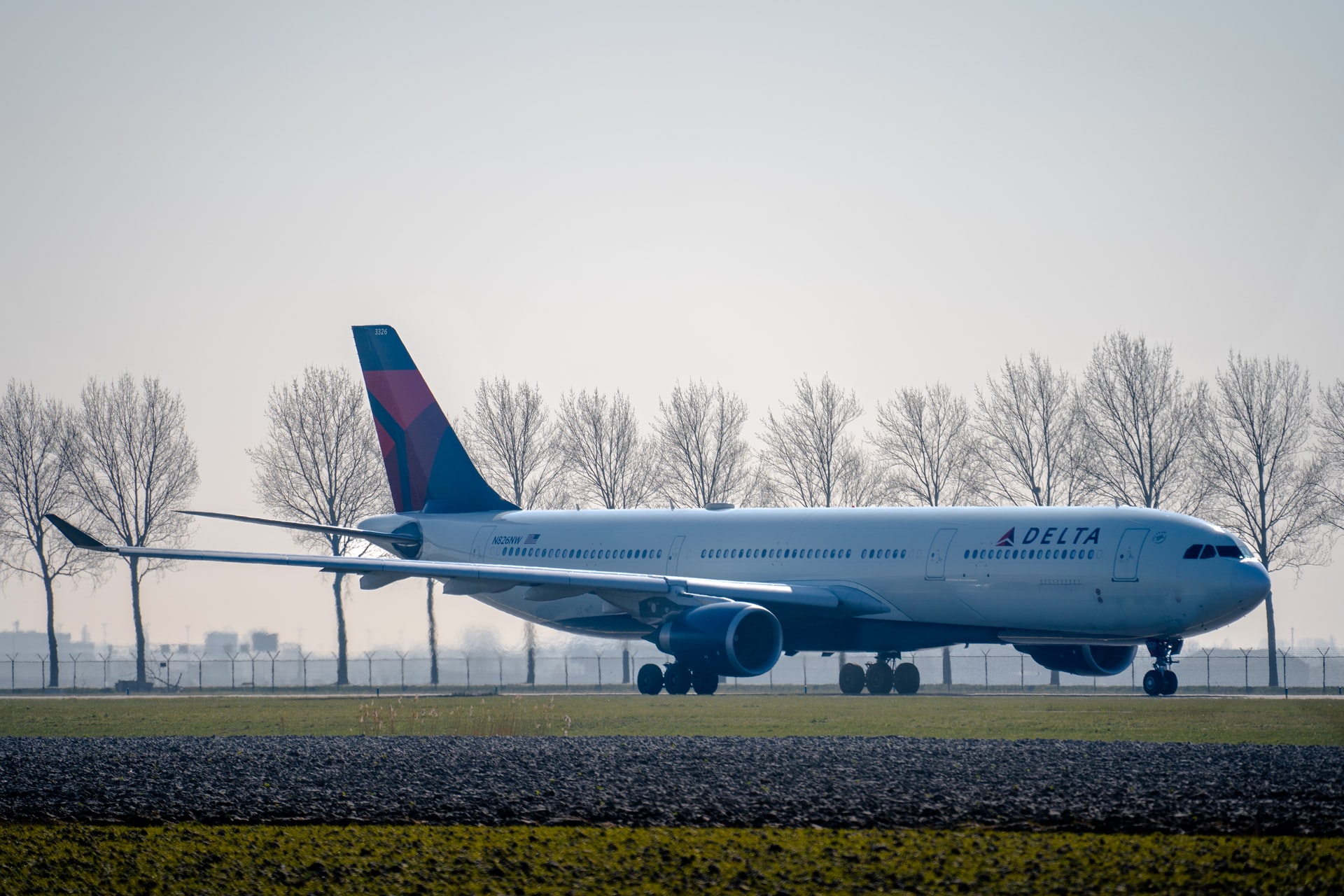 A Delta Airlines taxiing on a runway next to trees and grass.