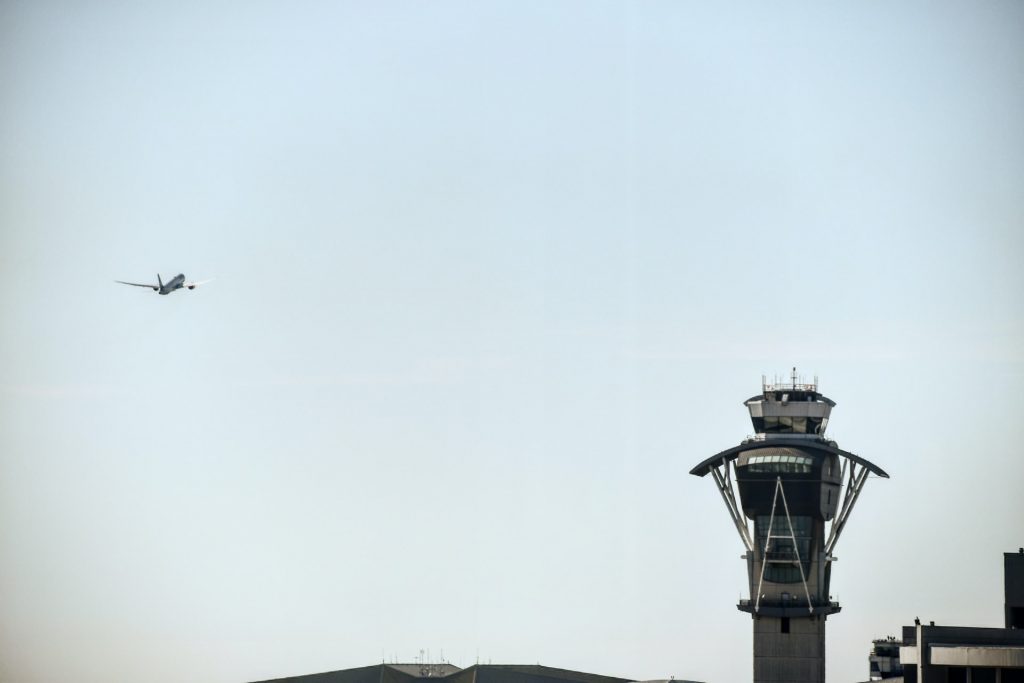 An ATC tower with an airplane approaching the runway in the distance.