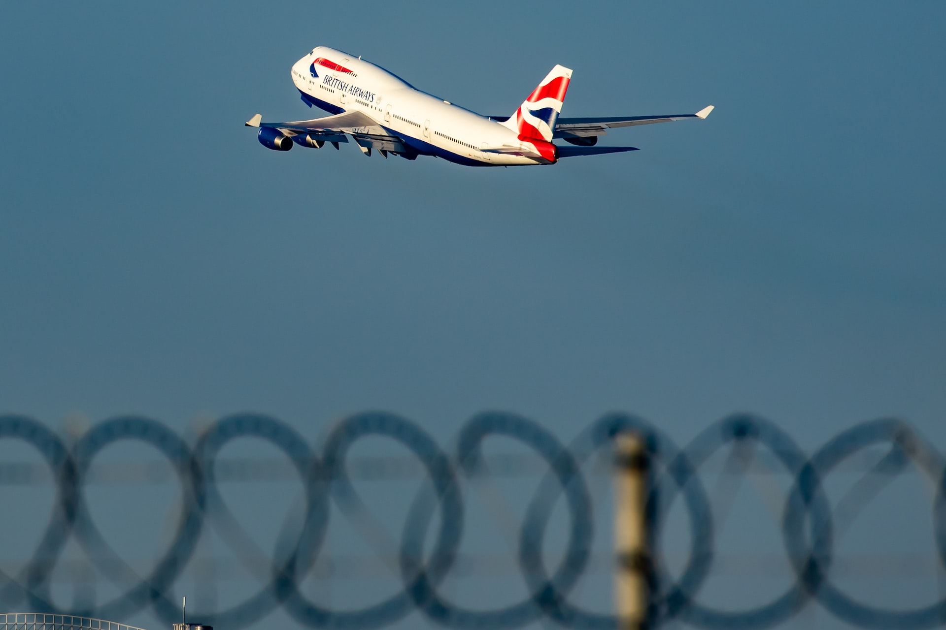 British Airways aircraft taking off from an airport behind a fence.