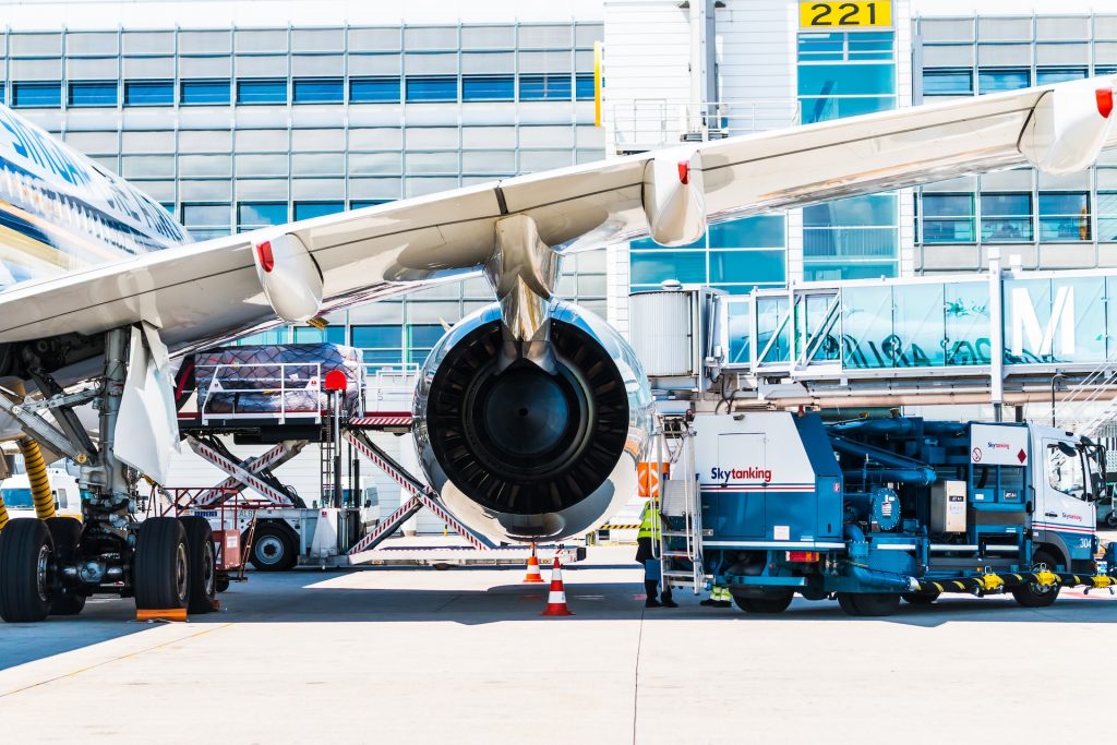 An aircraft fueler in a yellow vest fuelling an aircraft from a fuel truck.