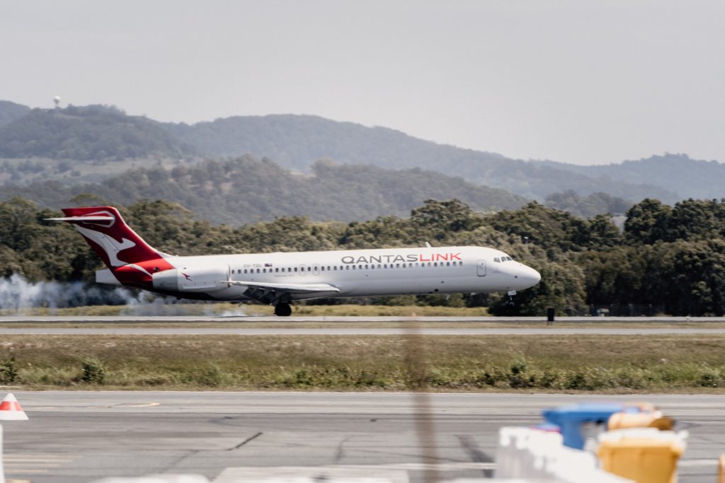 A white and red Qantas commercial aircraft landing on a runway.