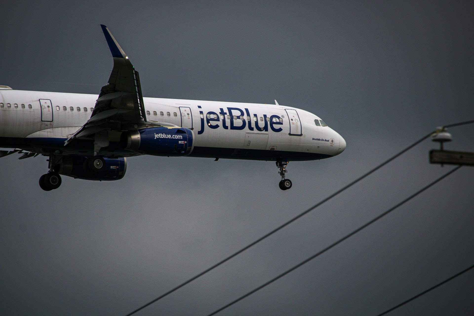 jetBlue aircraft landing over some electrical poles. 